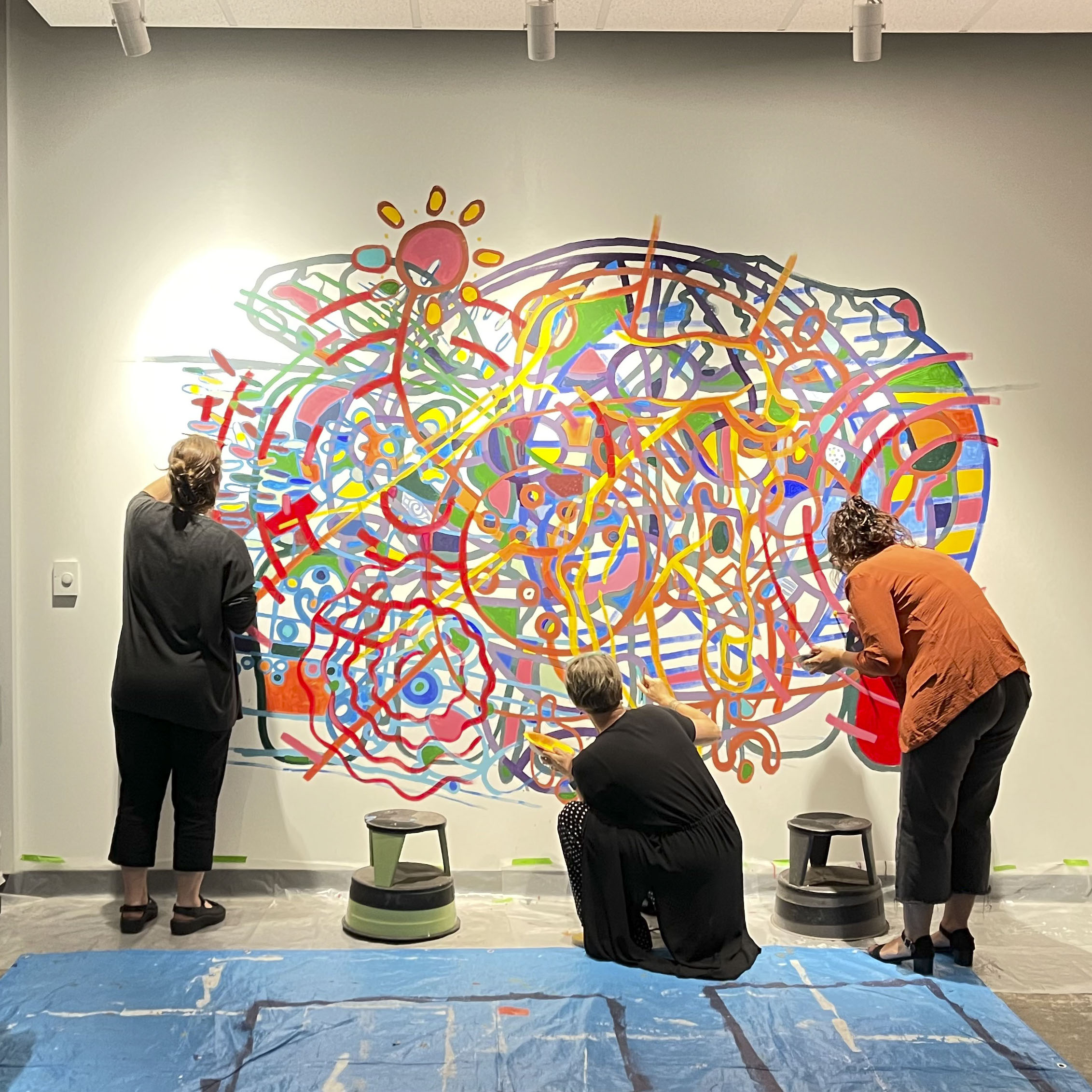 Three people painting a wall with colorful paint